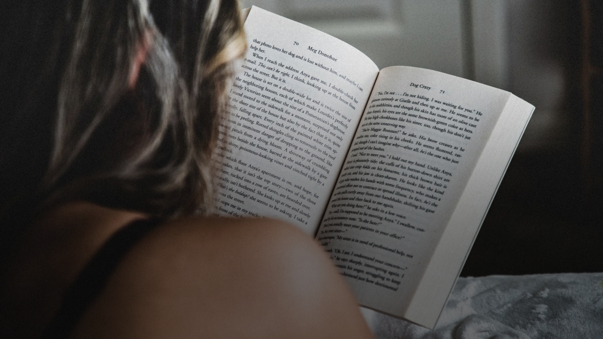 Woman reading a dark romance novel in bed, open book showing a tense confrontation scene — Forbidden Folio heat scale and content tracking for dark romance readers